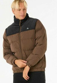 Bruine pufferjack met een zwart bovenstuk, hoge kraag en elastische manchetten. Voorzien van een ritssluiting en een klein logo op de borst.