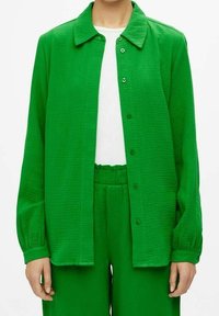 Chemise verte tissée avec fermeture à boutons sur le devant, col pointu et manches longues ; assortie à un pantalon vert assorti. Texture lisse.