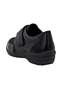 Chaussure en cuir noir avec un talon texturé et une sangle Velcro. Design arrondi, semelle légèrement rembourrée et construction de profil bas.