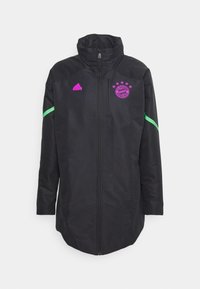 Veste longue noire avec fermeture éclair intégrale à l'avant, logo violet du FC Bayern Munich et logo Adidas, et bandes vertes sur les manches.