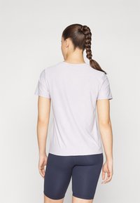 T-shirt viola chiaro a maniche corte con scollo rotondo e texture liscia, abbinato a pantaloni corti aderenti blu scuro. Vista posteriore mostrata.