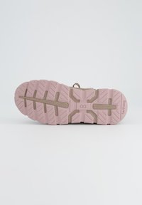 Semelle de chaussure avec une base en caoutchouc rose, dotée de crampons texturés et de rainures pour l'adhérence ; comprend une section beige et un détail de marque.