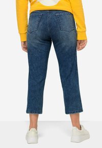 Pantalones de mezclilla cortos de cintura alta en azul oscuro con sutiles rayas verticales, con dos bolsillos traseros y un dobladillo sin acabar. Llevados con zapatillas blancas.