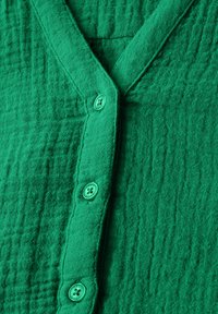 Camicia verde in cotone con bottoni, caratterizzata da un tessuto texturizzato, design a V e quattro bottoni coordinati lungo la parte anteriore.