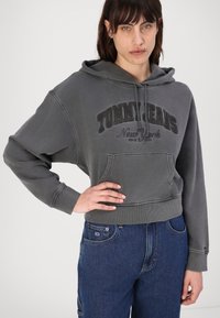 Felpa corta grigia con logo "TOMMY JEANS New York", tasca frontale e cappuccio con coulisse, abbinata a jeans di denim blu.