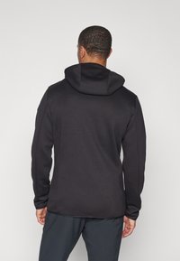 Svart hettegenser med en jevn tekstur, tettsittende design og lange ermer, med en kengurulomme og subtile sømmer.