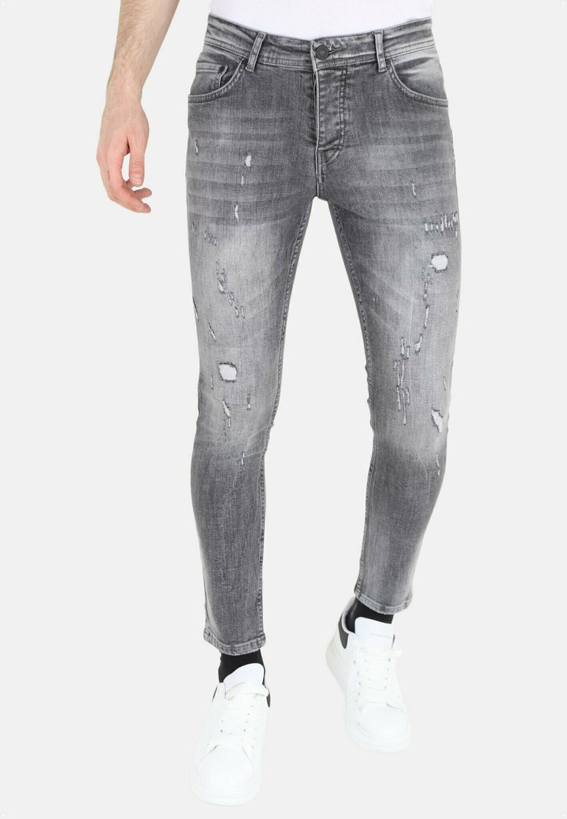 Slank gesneden grijze denim jeans met vervaagde plekken, versleten details en vijf-pocket ontwerp. Gepaard met witte sneakers.