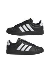 Baskets Adidas basses noires avec un design à trois bandes blanches et un patch au talon, lacets noirs et semelles en caoutchouc, vues de côté.