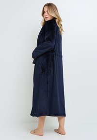 Robe long en bleu marine, douce, fabriquée en tissu pelucheux, avec un col, des poches latérales et une silhouette décontractée.