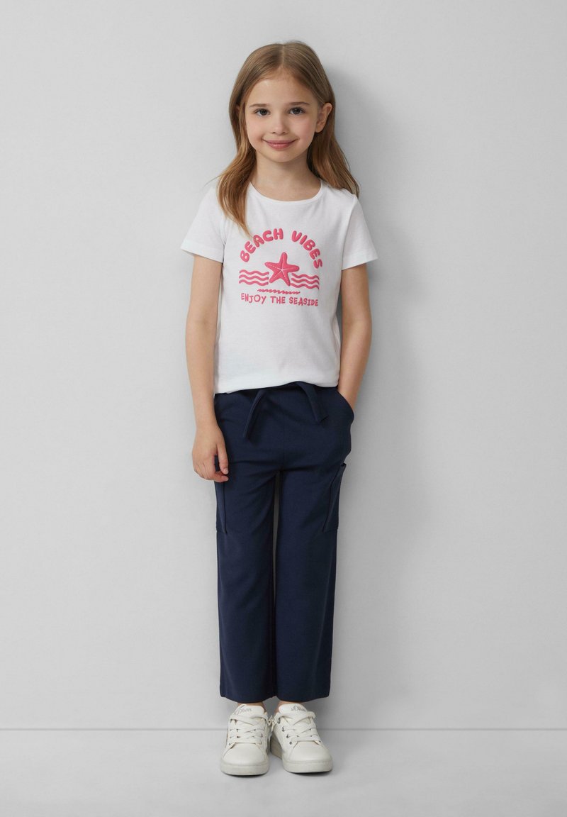 Witte katoenen t-shirt met roze opdruk met de tekst "Beach Vibes," gecombineerd met marineblauwe cargo broek en witte sneakers. Eenvoudig ontwerp en casual pasvorm.