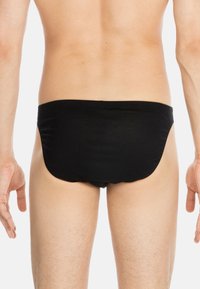 Schwarze Schwimmslips mit nahtlosem Design, elastischem Bund und glattem Stoff, von hinten betrachtet, wobei der untere Rücken und die Oberschenkel sichtbar sind.