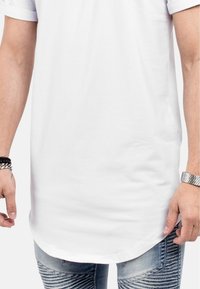 T-shirt en coton blanc avec un ourlet arrondi et des manches courtes retroussées, associé à un jean en denim bleu usé avec des détails de coutures horizontales.