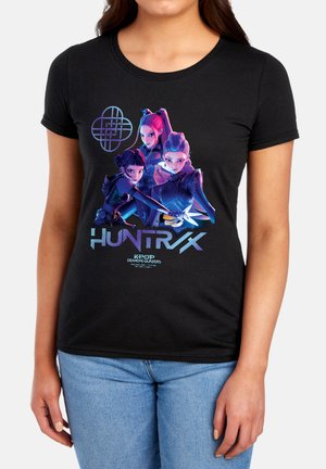 Woman wearing black shirt with glowing stylized illustration of three animated female characters and text "HUNTR/X K-POP Demon Hunters."