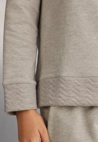 Lichtgrijze sweatshirt met ribbelmanchetten en een herringbone-tekstuur aan de onderrand. Zachte stof, ontspannen pasvorm, subtiele glans.