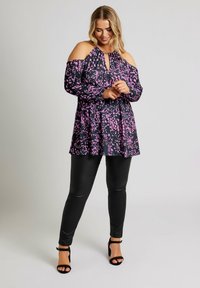 Top a spalle scoperte nero con motivo astratto rosa, scollatura a chiave, forma fluida, abbinato a pantaloni neri attillati simili alla pelle e tacchi neri.