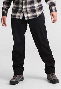 Czarne spodnie o luźnym kroju, wykonane z gładkiego, elastycznego materiału, z akcentem logo na udzie i zestawione z wytrzymałymi butami.