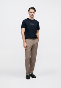 Μπλε μπλουζάκι με το λογότυπο 'Tommy Hilfiger', μπεζ παντελόνια, μαύρα μοκασίνια· απαλό ύφασμα, ορθογώνια εφαρμογή, κλασικό στρογγυλό γιακά, μινιμαλιστικός σχεδιασμός.