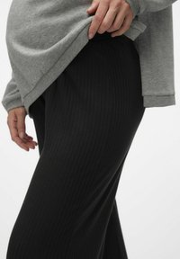 Pantalons noirs à côtes associés à une chemise à manches longues grise. La chemise a un ourlet arrondi et des manches ajustées, mettant en avant la texture et la simplicité.