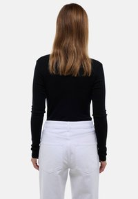 Un haut à manches longues noir associé à un pantalon blanc taille haute, avec deux poches arrière et une texture lisse, vu de dos.