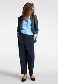 Groene blazer, lichtblauw gestreept shirt, marineblauwe broek en bruine platte schoenen; ontspannen pasvorm met opgerolde mouwen en omgeslagen broekspijpen.