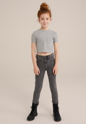 T-shirt grigia corta, jeans scuri a vita alta e stivali da combattimento neri con lacci. Tessuto di cotone liscio, vestibilità slim e design classico a cinque tasche.