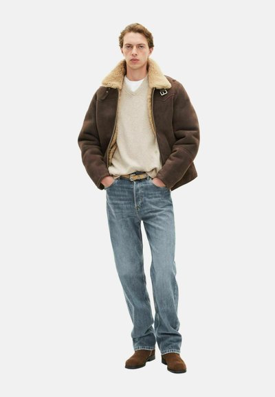 Chaqueta de shearling marrón, suéter beige, jeans azul claro y botas de ante marrones. Conjunto casual con un corte relajado y una paleta de colores naturales.