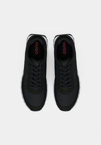 Pair of black Hugo sneakers with black laces and red "HUGO" branding inside the shoes, shown from top view on white background.