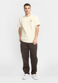 Cremefarvet bomuldstrøje med et lille blomstermønster; parret med løstsiddende mørkebrune bukser og hvide sneakers.