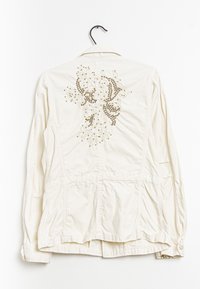 Bílá lehká bunda s detailním korálkovým designem na zadní straně, se šitými akcenty a dvěma předními kapsami.