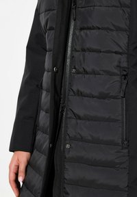 Giacca nera isolata con un design trapuntato, dotata di una chiusura frontale con zip e dettagli con bottoni. Il tessuto appare liscio e lucido.