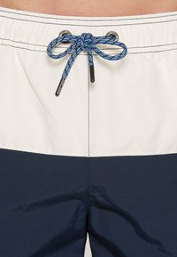 Plavky s bielo-námorníckym blokovým dizajnom, elastickým pásom s modrou šnúrkou na stiahnutie a striebornými očkami na úpravu.