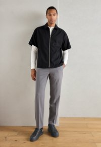 Cămașă scurtă neagră cu fermoar, pantaloni gri ajustați și adidași negri. Material neted, croială casual, cu un design minimalist.