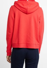 Sudadera de forro polar roja con capucha ajustable, puños y dobladillo acanalados. Textura suave, corte casual y diseño corto.