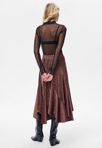 Przezroczysta czarna bluzka z długim rękawem w połączeniu z metaliczną, brązową, rozkloszowaną spódnicą o teksturowanym, błyszczącym wykończeniu oraz czarne botki na obcasie sięgające kostek.