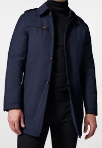 Manteau d'extérieur bleu marine avec fermeture à boutons, épaulettes détaillées et col classique. Texture lisse avec une coupe droite.