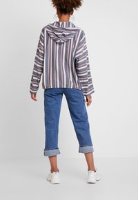 Gestreifter Hoodie mit grauem Grundton, weißen und korallenfarbenen Linien, langen Ärmeln und Kapuze mit Kordelzug, kombiniert mit hochgerollten blauen Jeans und weißen Turnschuhen.