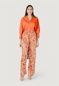 Een oranje overhemd met knopen, gecombineerd met oranje en witte wijde broeken met een patroon, voorzien van een trekkoord in de taille en een bloemmotief.