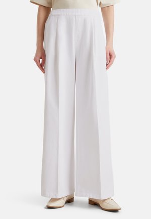 Pantalons blancs à jambes larges, confectionnés dans un tissu léger et à la texture lisse ; dotés d'une taille haute et de lignes épurées. Associés à des chaussures beiges.