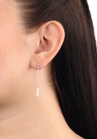 Orecchini pendenti caratterizzati da una catena argentata e tre perle bianche. Design minimalista con una leggera lucentezza e una texture liscia.