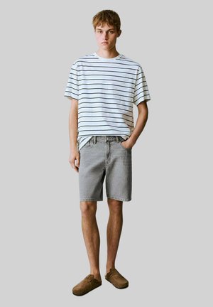 T-shirt à manches courtes rayé en blanc et marine, associé à un short en denim gris et des chaussures à enfiler marron. Coupe décontractée et style relax.