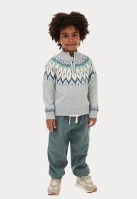 Maglione lavorato a maglia color grigio chiaro con un colletto decorato in blu e verde. Abbinato a pantaloni larghi color teal e sneakers beige.