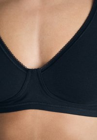 Crni meki materijal bralette s V-izrezom, ukrasnim picot rubom i glatkim šavovima za čistu završnicu. Središnje nabrane za oblikovanje.