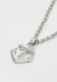 Silver anchor pendant necklace with a polished finish, featuring a chain link design and four curved prongs at the base of the anchor.