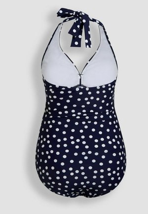 Maillot de bain une pièce bleu marine avec des pois blancs, design à nouer autour du cou, dos décolleté, et doublure blanche contrastante.