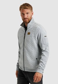 Grijze gewatteerde zip-up jas van zacht materiaal, met een hoge kraag, zijzakken en een klein embleem op de borst.
