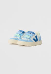 Sinine ja helesinine velcro rihmadega sneakerid, samet- ja nahkmaterjalid, tekstuuriga valge tald ning eristuv logo külgedel.