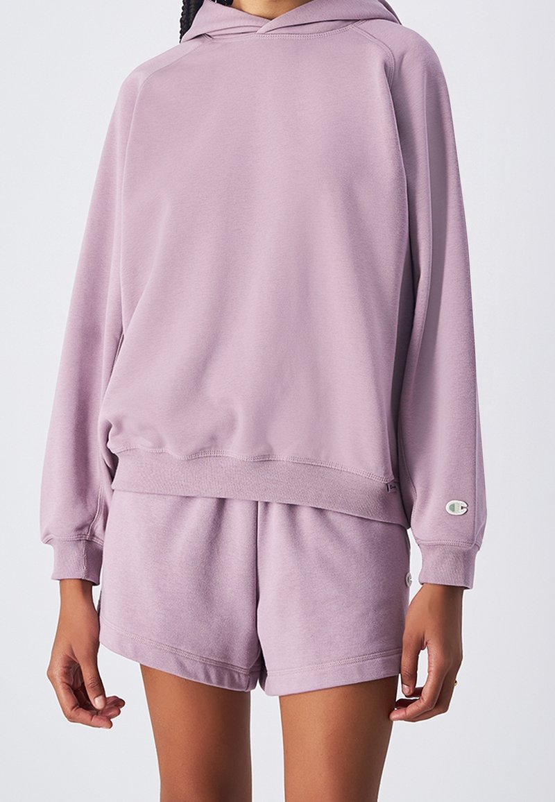 Felpa viola chiaro con cappuccio regolabile, polsini e orlo a coste, abbinata a pantaloni corti coordinati. Tessuto morbido e testurizzato. Logo Champion sulla manica.