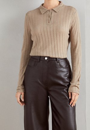 Beige geribbelde poloshirt met lange mouwen en drie knopen; gecombineerd met hoge, donkerbruine wijde faux leren broek.