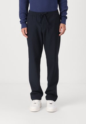 Marineblå elastiske sweatpants med snor i taljen, der har en afslappet pasform og glat stoftekstur, kombineret med hvide sneakers.