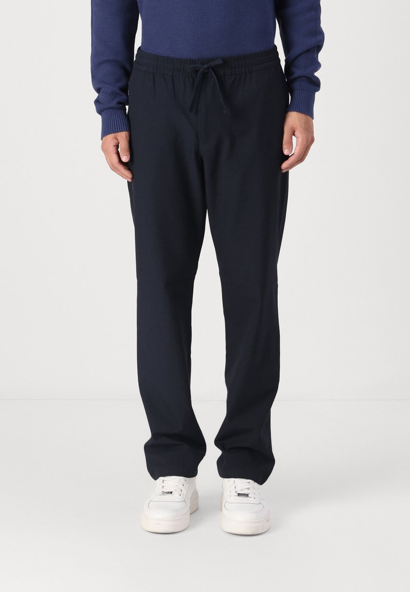 Marineblå elastiske joggebukser med snøring i midjen, med en avslappet passform og glatt stofftekstur, parret med hvite sneakers.